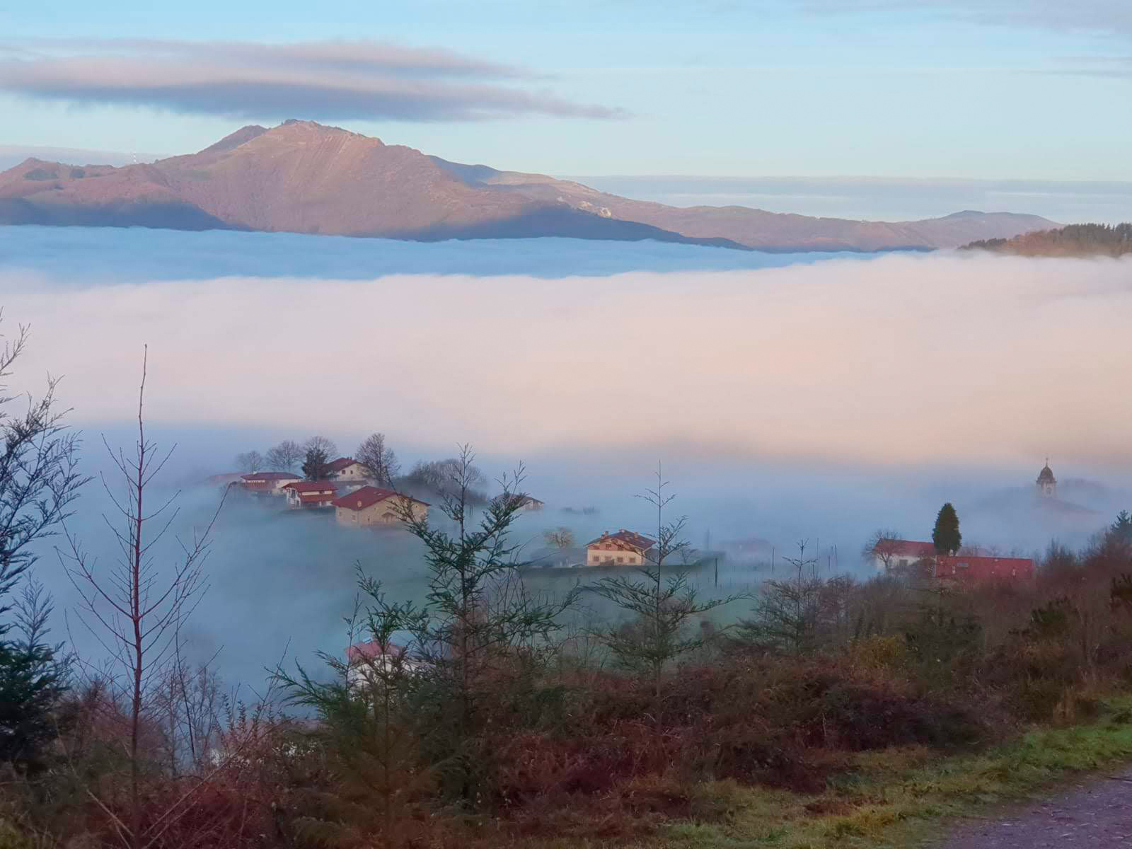 paisaje montana niebla araceli vazquez irun - Araceli Vázquez Psicóloga en Irún Paisaje de montaña con casas parcialmente cubiertas por la niebla al amanecer, simbolizando claridad y orientación en el proceso terapéutico guiado por Araceli Vázquez en Irún